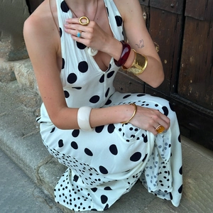 Detail shot of a white polka dot maxi dress with elegant accessories on a model seated outdoors
