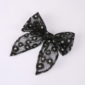 Detail of a large black lace bow hair clip with delicate white floral embroidery