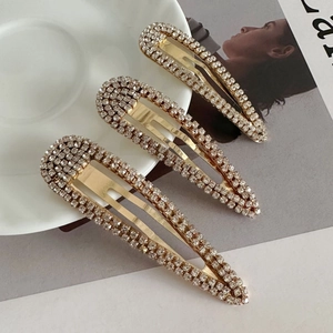 Close-up of three gold-plated drop-shaped hair clips with sparkling crystal rhinestones