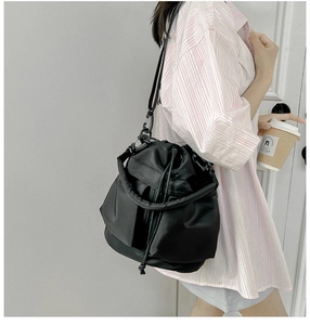 Close-up of black nylon drawstring bucket bag with thick handle shown on model