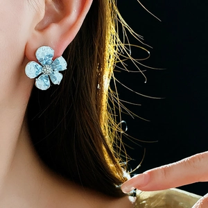 Macro shot of gradient blue flower earring with crystal center worn by a model