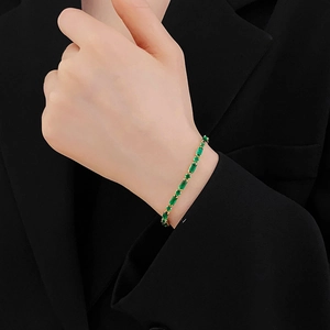 Primer plano de pulsera bañada en oro con circonitas verde esmeralda en la muñeca