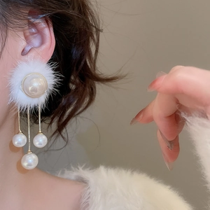 Detail of white pom-pom earrings with dangling pearl tassels worn on a model ear