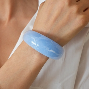 Detailed view of wide light blue resin bangle with marble texture on model's wrist