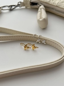 Close-up of abstract knot earrings in polished gold and silver finishes on beige leather