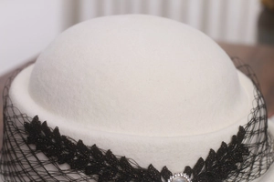 Détail du béret en laine blanche avec maille de dentelle noire et broche en perles