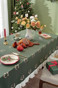 Detailed close-up of green cotton tablecloth with Christmas embroidery and white ruffles