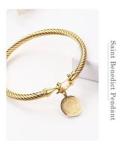 Macro shot of gold St. Benedict medal on a twisted wire cable bangle with U-shaped clasp