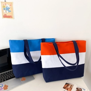 Detailed view of striped canvas tote bags in blue and orange on a desk with a laptop