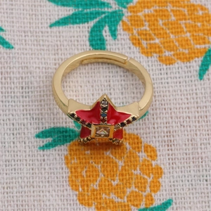 Detailed close-up of a golden adjustable star ring with red enamel and central zircon