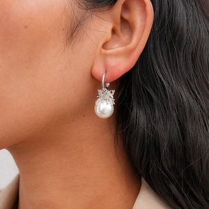 Detail of a C-shape silver earring featuring a unique pearl spider pendant on a model