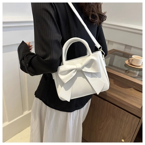 Close-up of white faux leather bucket bag with large bow detail and gold hardware