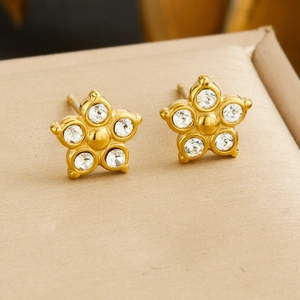 Close-up of gold flower stud earrings with sparkling clear crystals on beige background