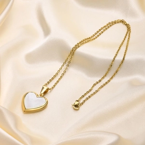 Detail of a gold heart locket necklace with white shell inlay on champagne silk fabric