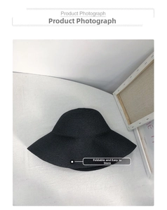 Close-up of foldable black woven sun hat showing detailed straw texture on white background