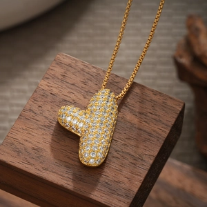 Close-up of 18K gold letter T pendant with shimmering pavé zircon on dark wood