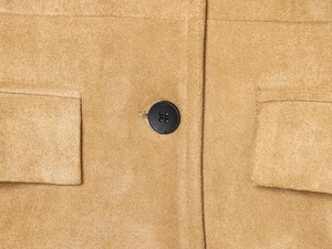 Détail d'un blazer en daim kaki montrant la texture, le bouton noir et le rabat de poche