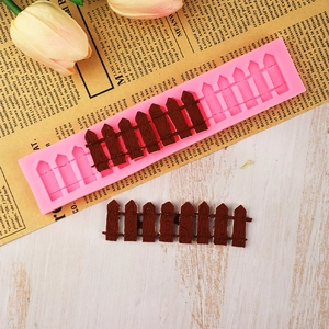 Pink silicone garden fence mold with brown chocolate fence pieces on wooden background