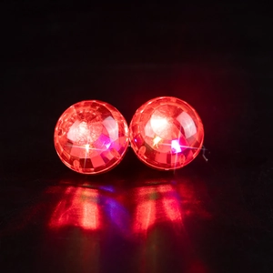 Close-up of glowing red disco ball earrings on a reflective black surface with light effect