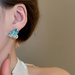 Detail of 18k gold-plated earrings featuring square green crystals and pearls on model