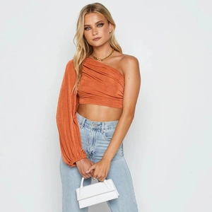 Détail du haut court orange à une épaule en tissu plissé brillant avec manche longue