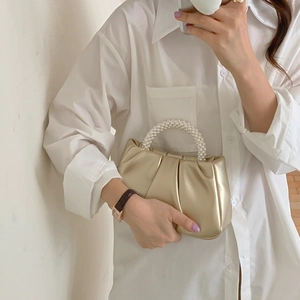 Detail of gold pleated cloud handbag featuring elegant pearl handle held by a model