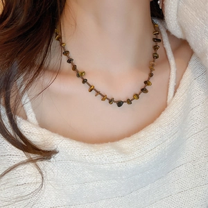 Détail d'un collier en pierre d'oeil de tigre porté sur un pull en maille blanc