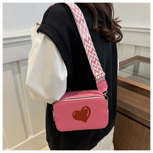 Pink heart camera bag with textured leather and geometric woven strap in front view