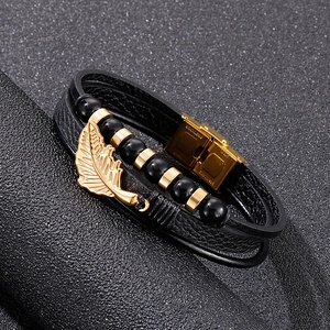 Detailed close-up of double-layer black leather bracelet with golden feather pendant