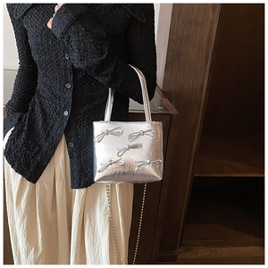 Detail of silver handbag featuring decorative bows and a stylish metal chain shoulder strap