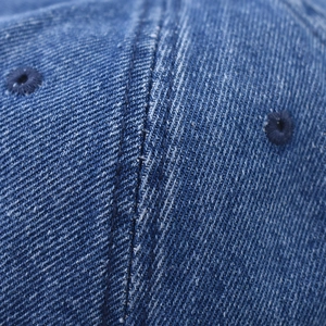 Macro detail of dark blue washed denim fabric with stitched eyelets on a baseball cap