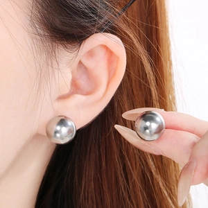 Close-up of a model wearing and holding silver hollow spherical stainless steel earrings