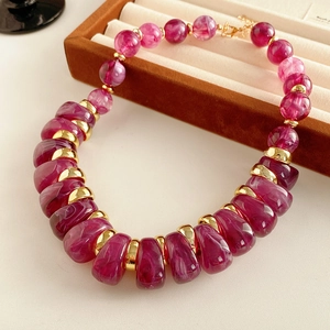 Détail de perles en résine marbrée violette et anneaux dorés sur un collier vintage
