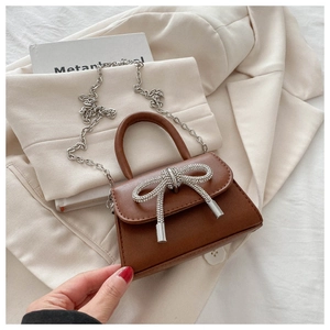 Close-up of brown mini handbag featuring a rhinestone bow and silver chain strap