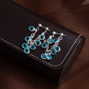 Elegant silver tassel earrings with sky blue crystal pendants on a brown leather jewelry box