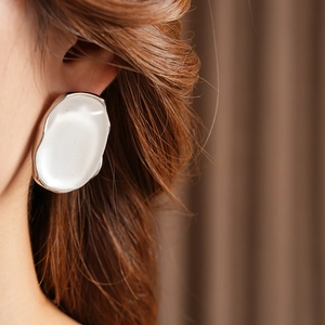 Close-up of minimalist large oval silver earrings on model with elegant matte texture