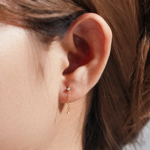 Close-up of gold chain cartilage earrings with clear crystals on model ear