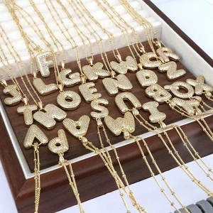 Gold plated initial pendant necklaces with cubic zirconia pavé on a wooden jewelry tray