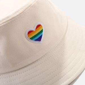 Nahaufnahme der Regenbogen-Herz-Stickerei auf dem beigen Fischerhut aus Baumwolle