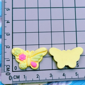 Detailed view of yellow resin butterfly charms with size measurements on a grid mat