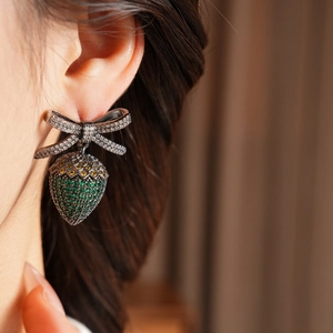 Macro side view of a vintage bow strawberry earring set with sparkling green cubic zirconia