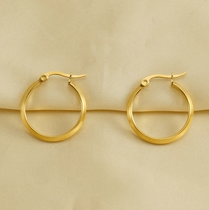 Detail von 18K vergoldeten Edelstahl-Creolen auf weichem beige-farbenem Stoffhintergrund