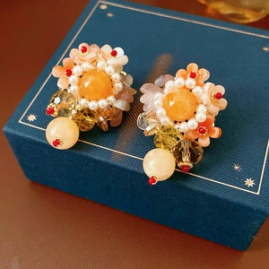 Détails de boucles d'oreilles fleuries avec perles orange et cristaux jaunes sur boîte