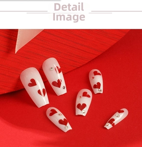 Detail of medium-long press-on nails with red heart patterns and small rhinestones