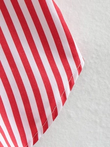 Detail of red and white striped poplin shirt showing precision stitching on the hemline