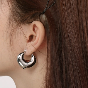 Close-up of polished silver oval hollow hoop earrings worn by a model in a minimal style