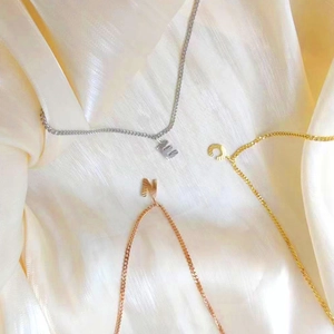 Detalle de colgantes de letras en oro, plata y oro rosa sobre fondo de seda suave