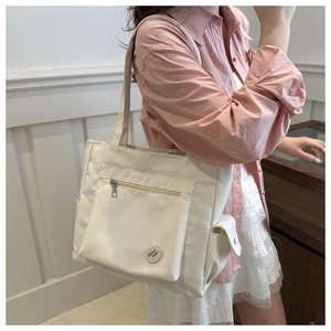 Close-up of a cream nylon tote bag featuring a front zipper pocket and side flap pocket
