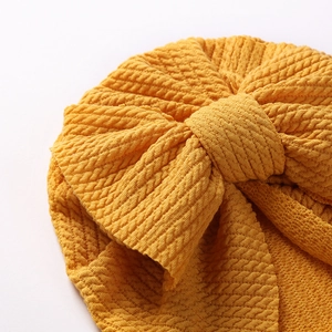 Macro shot of ginger yellow ribbed knit baby turban featuring a large textured bow