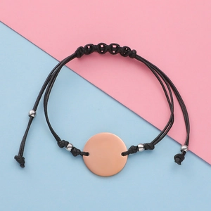 Macro shot of polished rose gold round metal plate on black adjustable woven cord bracelet